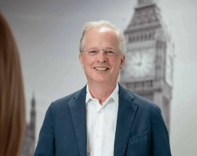Smiling man in a blue blazer standing in front of a blurred image of Big Ben.