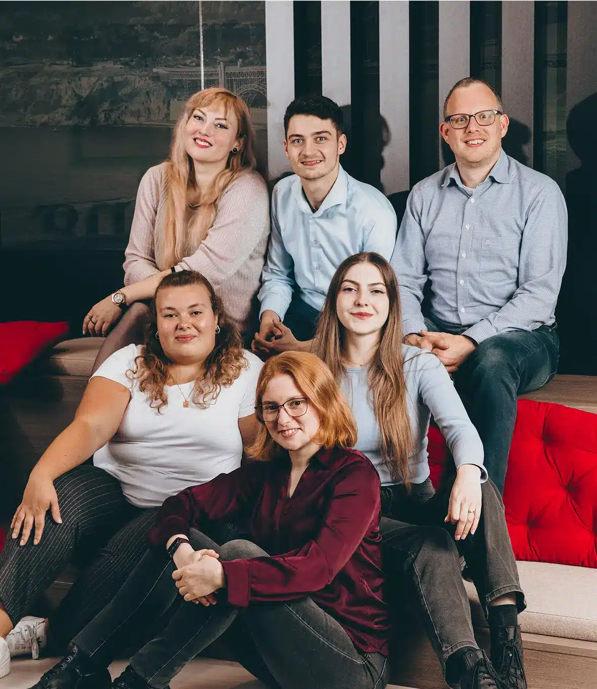 Group photo of six smiling team members sitting and posing together indoors.