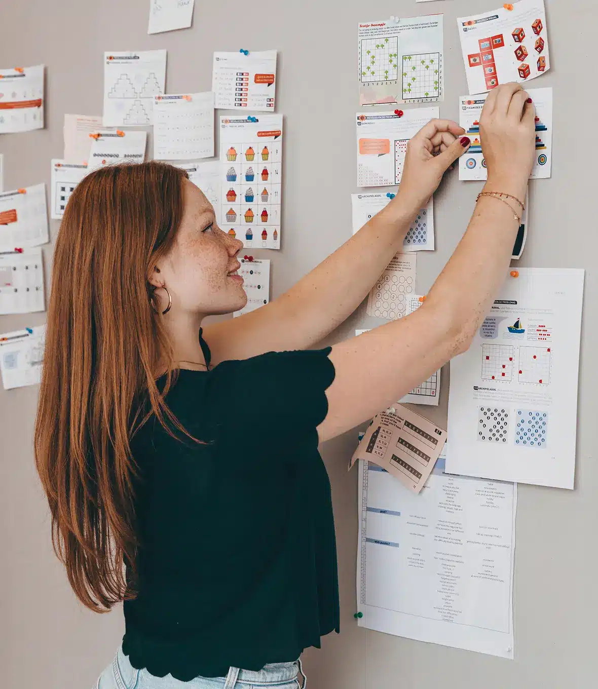 Woman pinning colorful educational worksheets to a wall-mounted pin board.